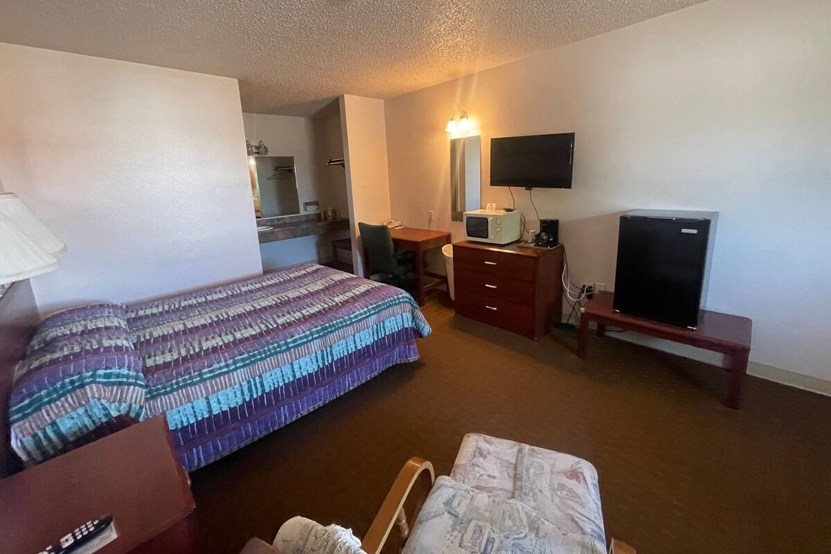 A hotel room with a bed, a desk, a television, and a microwave.