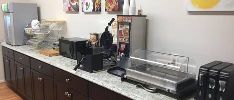 Una cocina con un maker de gofres, una cafetera y un expositor de alimentos.