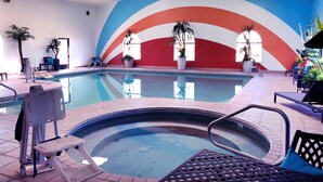 An indoor swimming pool with a colorful mural, lounge chairs, and potted plants. - Navajoland Inn (St. Michaels)