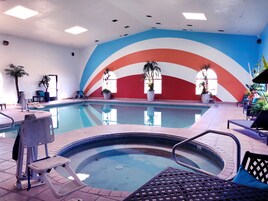 Una piscina interior con un mural colorido, sillas de descanso y plantas en macetas.