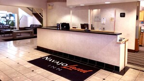 A reception desk with a digital clock, a laptop, and a coffee machine. There is a reception area with a counter and a mirror above it. - Navajoland Inn (St. Michaels)