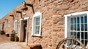 A stone building with multiple windows and doors, barrels outside, and a wooden wheel. - Navajoland Inn (St. Michaels)