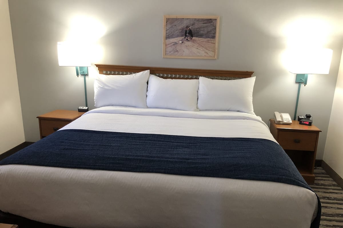 Et hotelværelse med en stor seng, to sengeborde, et natbord med telefon og vækkeur, samt to væglamper.