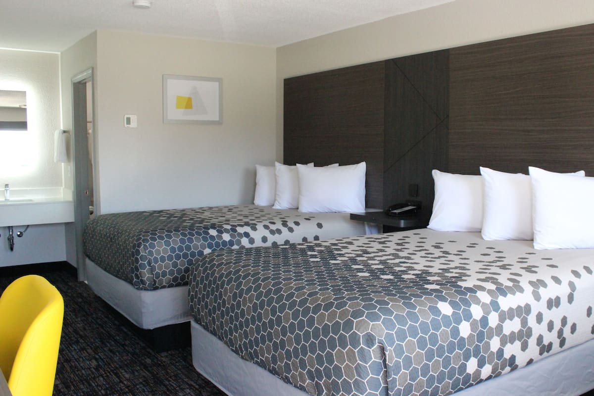 A hotel room with two beds, a desk, a chair, and a large window.