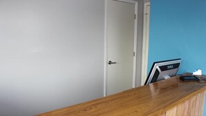 Un comptoir d’accueil en bois, une porte blanche fermée et un mur bleu.