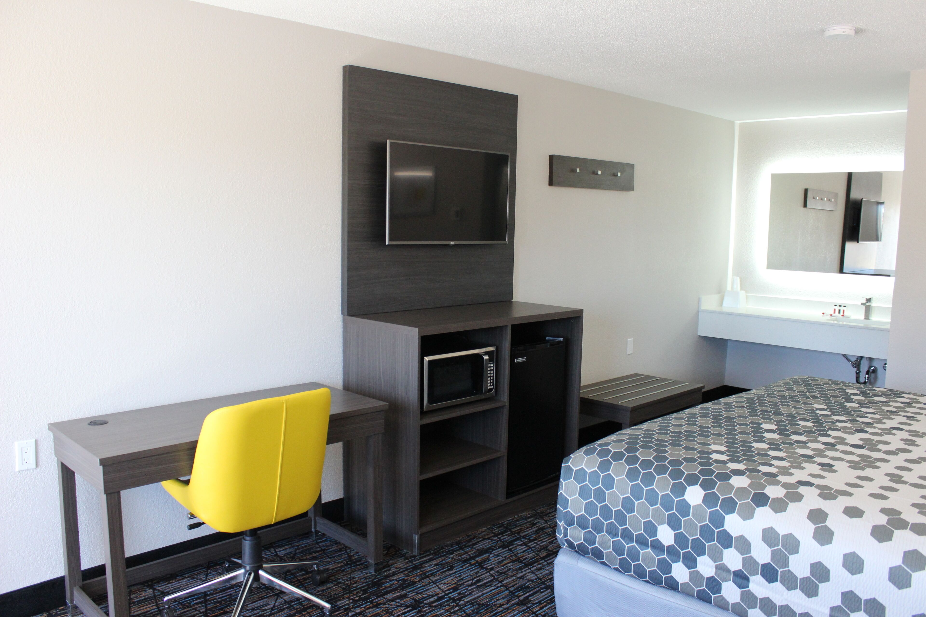 A hotel room with a bed, a desk with a chair, a TV, a microwave, and a sink.