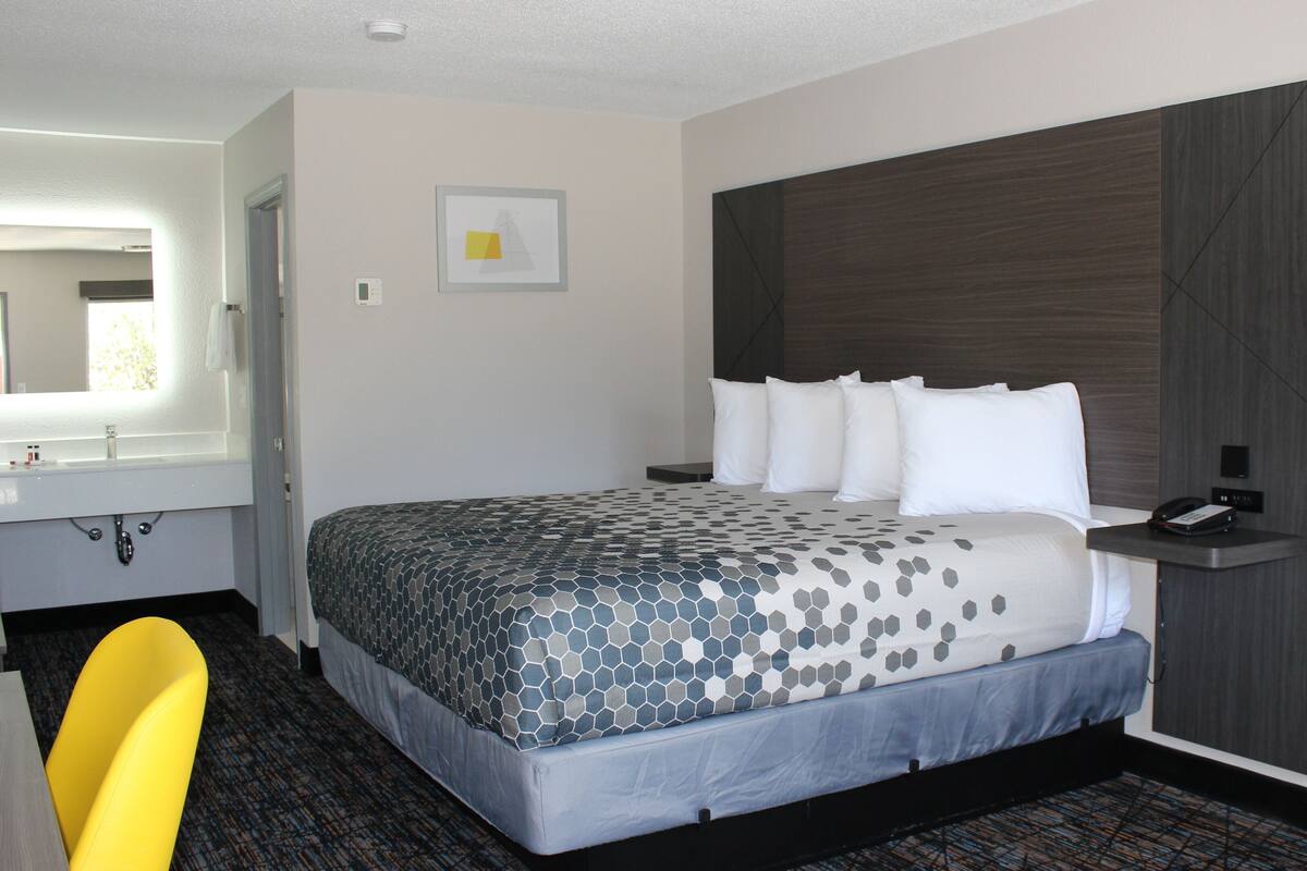 A hotel room with a large bed, a bedside table with a phone, a mirror, and a bathroom with a sink and toilet.