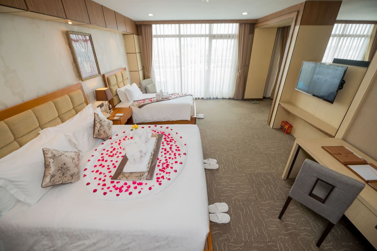 A hotel room with two beds, a desk, a TV, and a shower area.