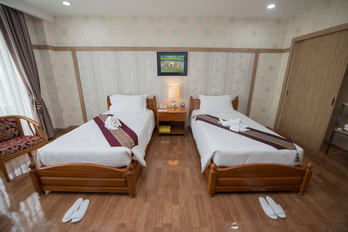 A hotel room with two wooden beds, a nightstand, a lamp, a framed picture on the wall, and a wooden wardrobe.