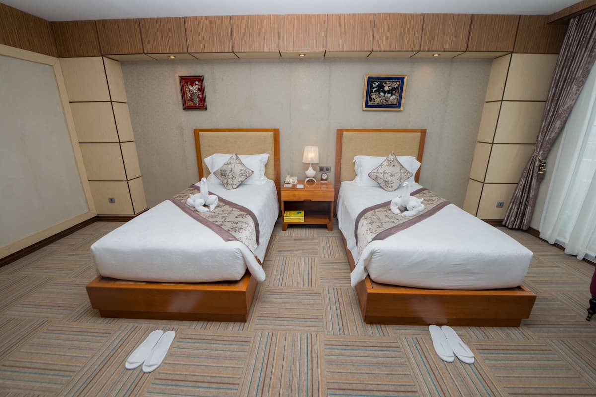 A hotel room with two beds, a nightstand, and a small table.