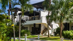 A modern building with a covered outdoor area, palm trees, and a pathway. - Aligio Aparthotel & Spa (Las Terrenas)
