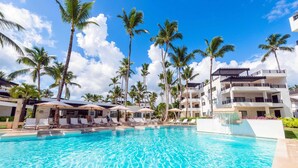 A swimming pool with lounge chairs and umbrellas, surrounded by palm trees and a multi-story building. - Aligio Aparthotel & Spa (Las Terrenas)