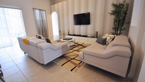 A modern living room with two white sofas, a coffee table, a flat-screen TV, and a large plant. - Solterra Resort (Davenport)