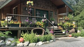 A log cabin with a porch decorated with hanging flower baskets and potted plants. - Twin Peaks Lodge and RV Park (Seward)