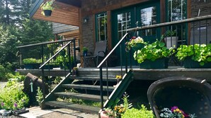 A wooden staircase leading to a stone building with a green door, outdoor seating, and potted plants. - Twin Peaks Lodge and RV Park (Seward)