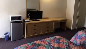 A hotel room with a bed, a desk with a computer and a microwave, a dresser, and a door. - Colonade Motel (Hightstown)