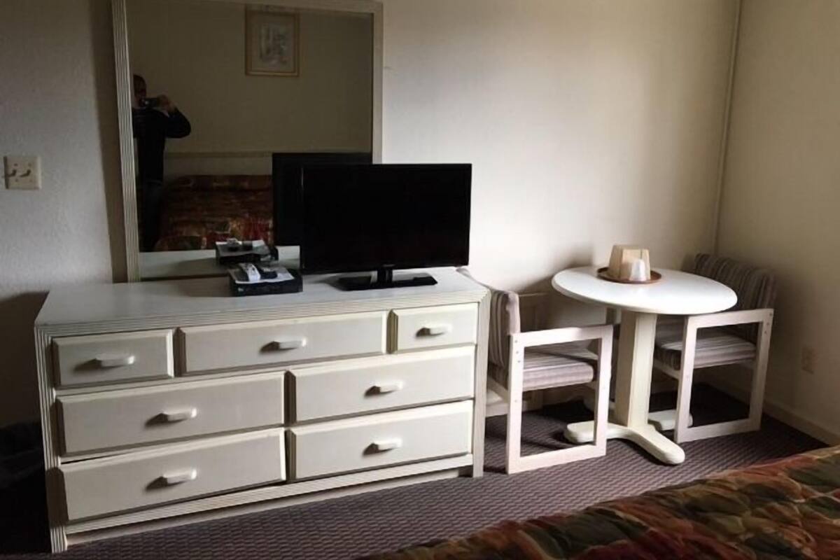 A hotel room with a white dresser, a television, a small round table, and a chair.
