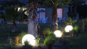 A garden area with palm trees, a patio with chairs, and spherical lights. - Apart Hotel Gran Pacifico (La Serena)
