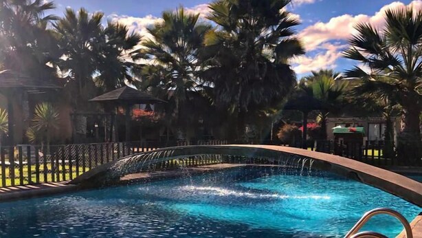 A swimming pool with clear blue water, surrounded by palm trees and a stone deck. - Apart Hotel Gran Pacifico (La Serena)
