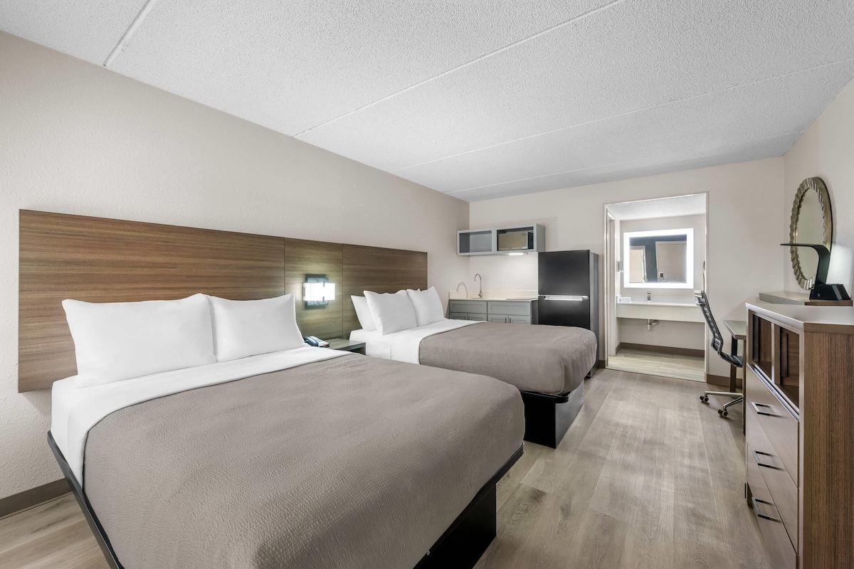 A hotel room with two beds, a desk, a chair, a TV, a mirror, and a wardrobe.