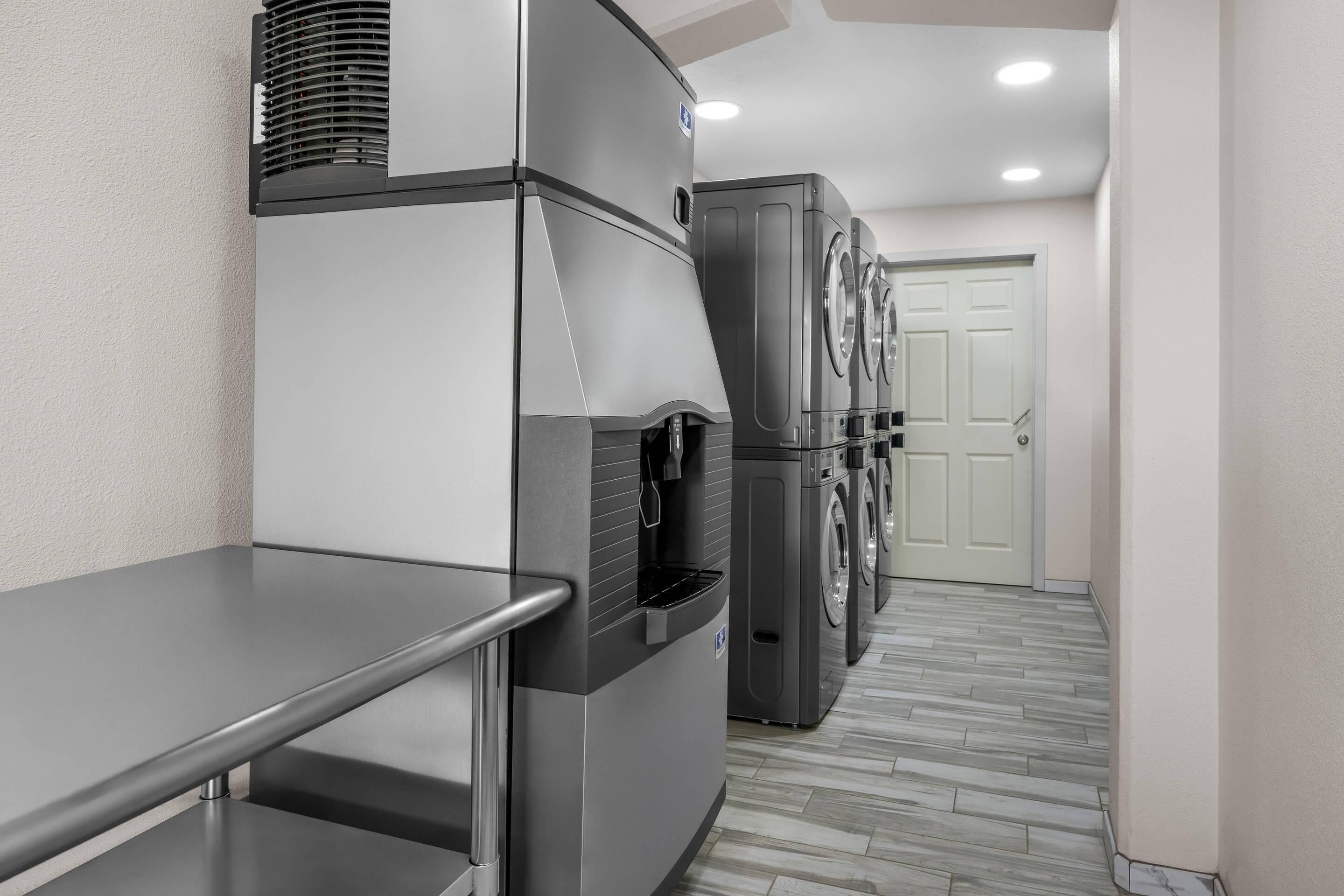 A laundry facility with a metal table, a large refrigerator, and stacked washing machines.
