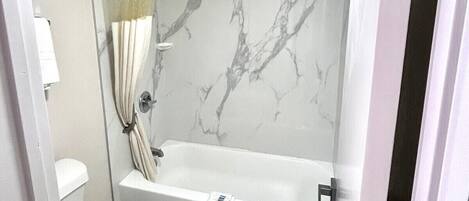 Une salle de bain avec un mur de douche en marbre, une baignoire et des toilettes.