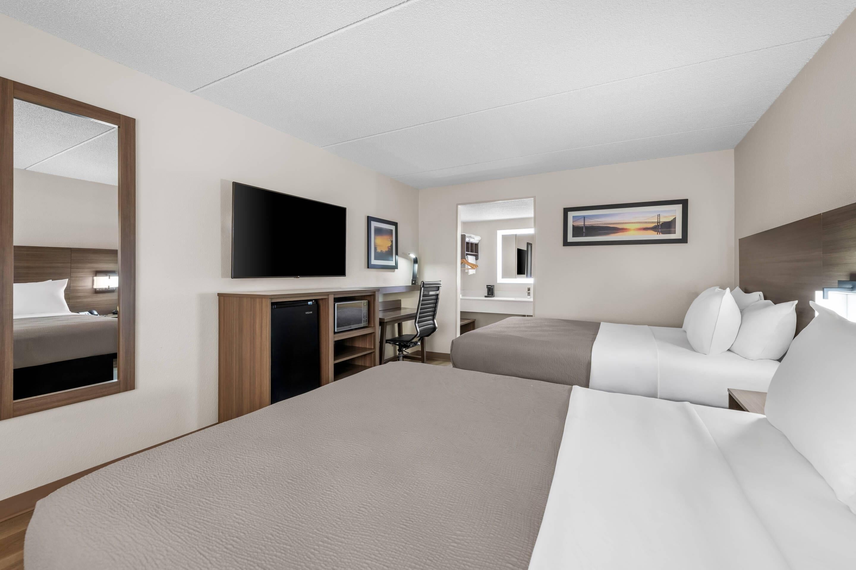 Habitación de hotel con una cama grande, un escritorio con computadora, televisor y espejo.