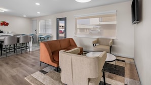 A modern living room with a sofa, chairs, a dining area, and a TV mounted on the wall.