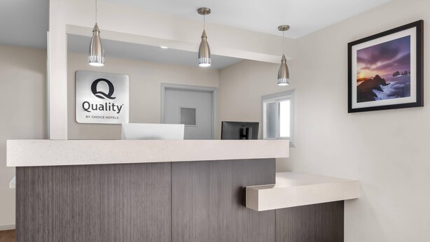 A hotel reception desk with a 'Quality by Choice Hotels' sign, pendant lighting, and a framed picture on the wall.