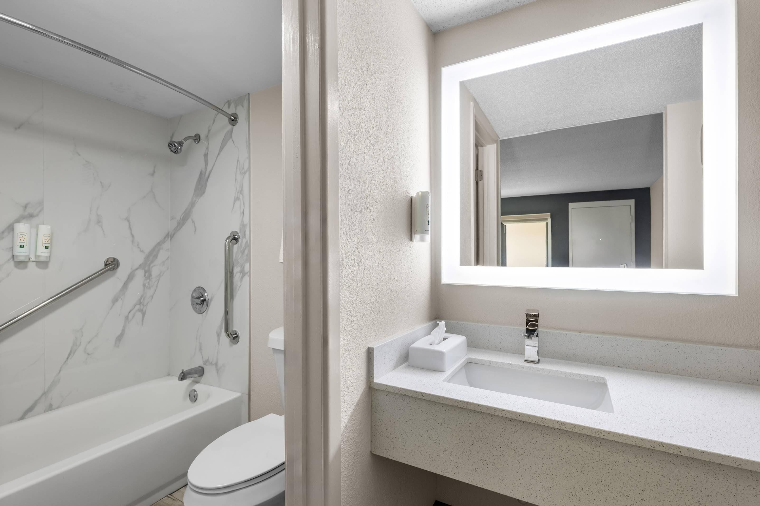 A modern bathroom with a bathtub, toilet, and a large mirror above the sink.
