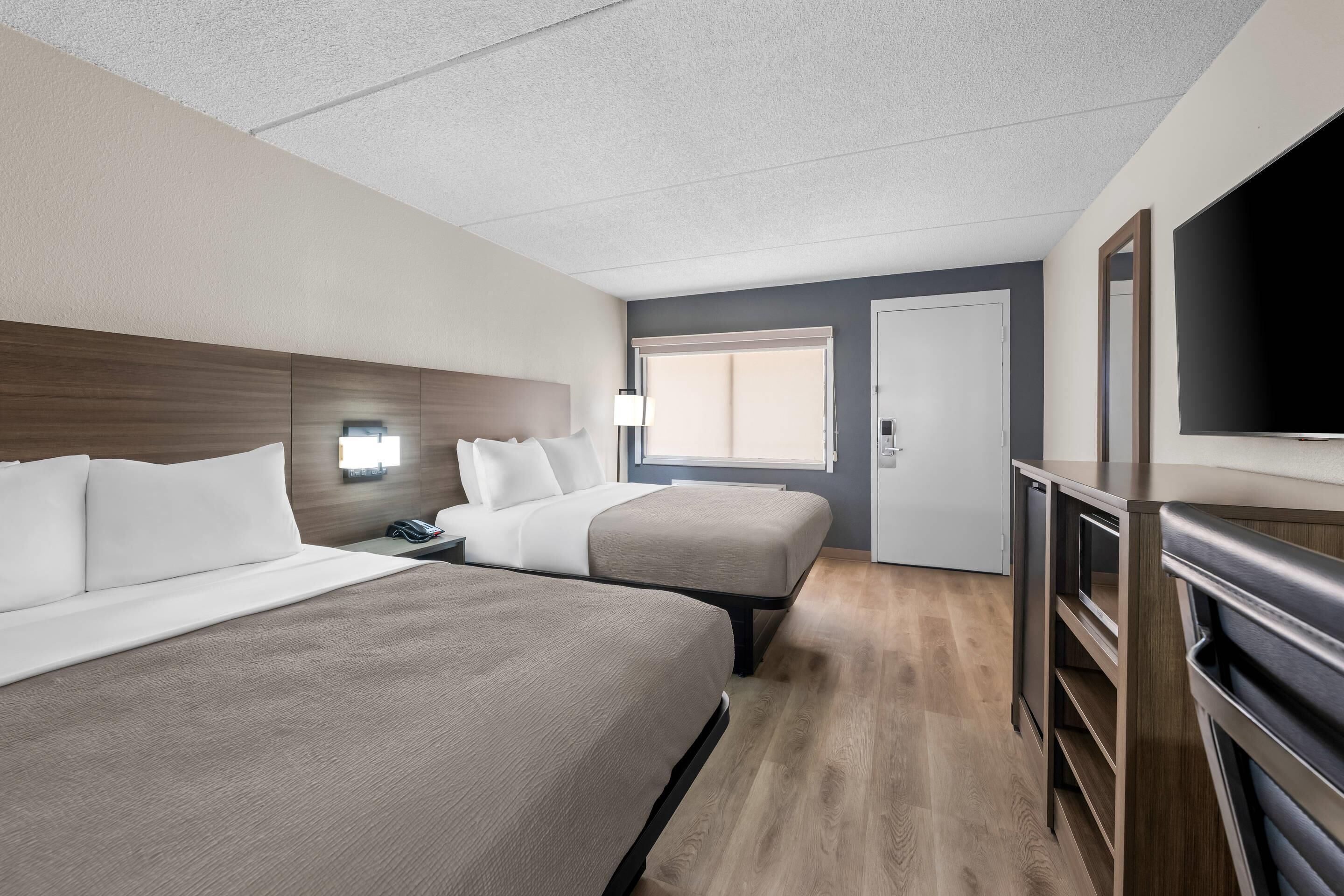 Habitación de hotel con dos camas, televisión, escritorio y ventana.
