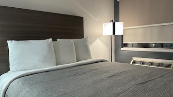 Une chambre d’hôtel avec un lit, une table de chevet, une lampe et une fenêtre avec des stores.