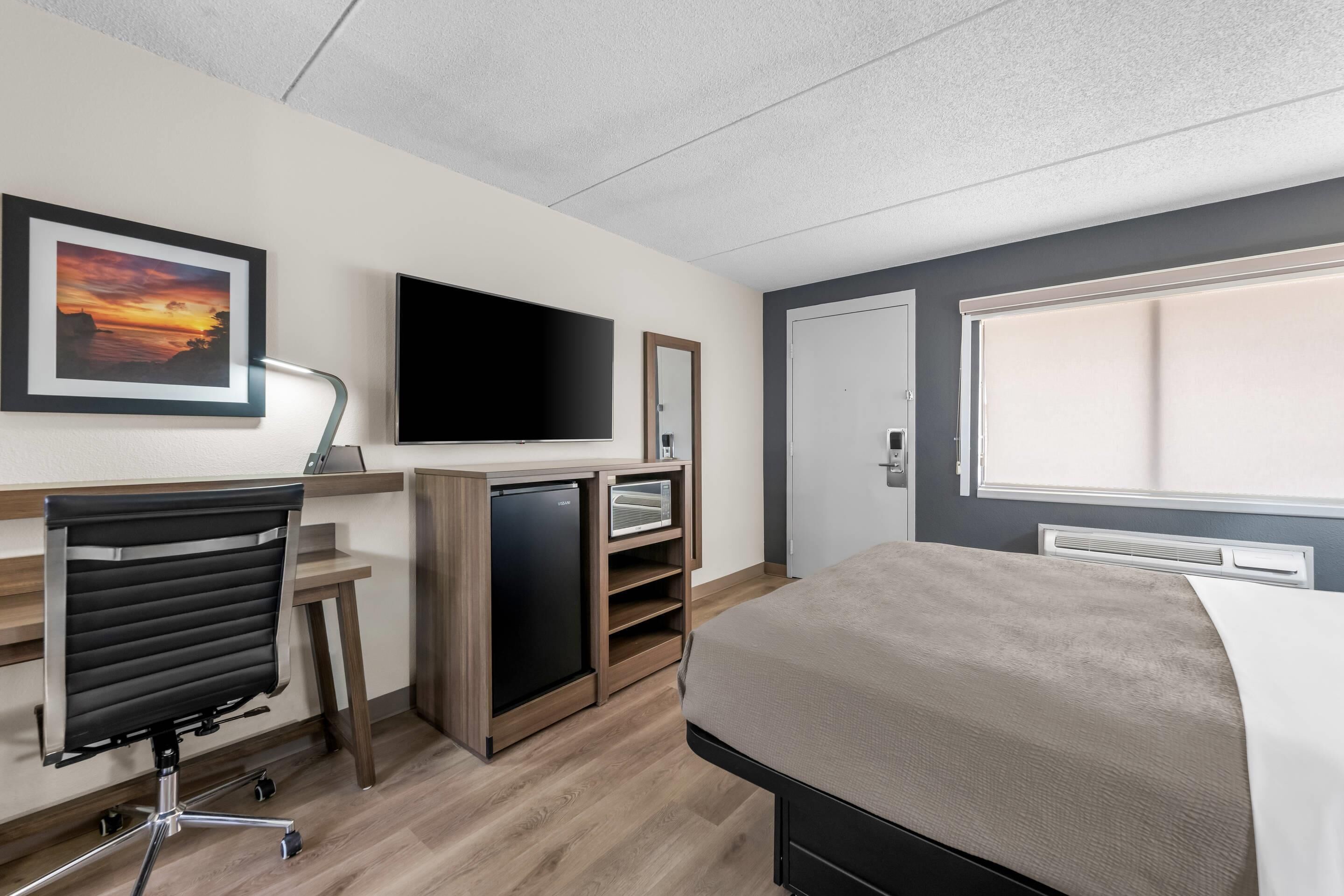 Une chambre d’hôtel avec un lit, un bureau, une chaise, une télévision et une porte.