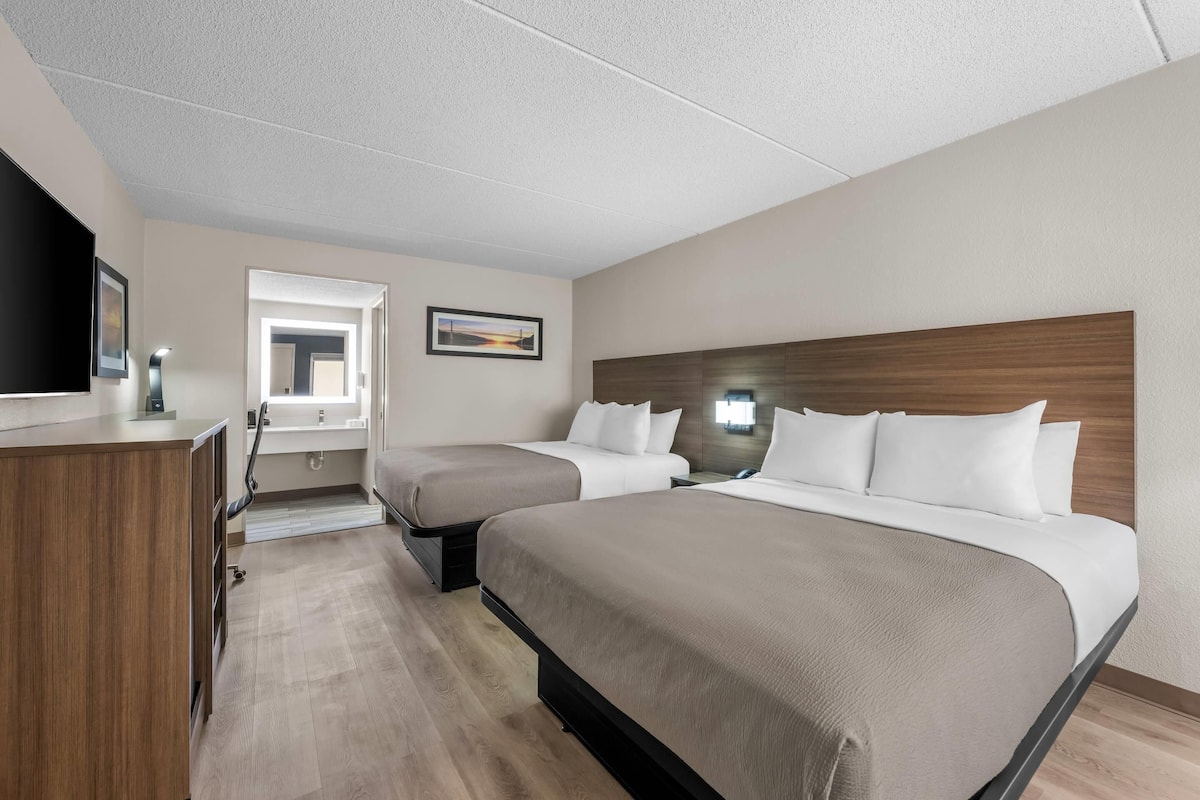 A hotel room with two beds, a desk, a TV, and a window with a view.