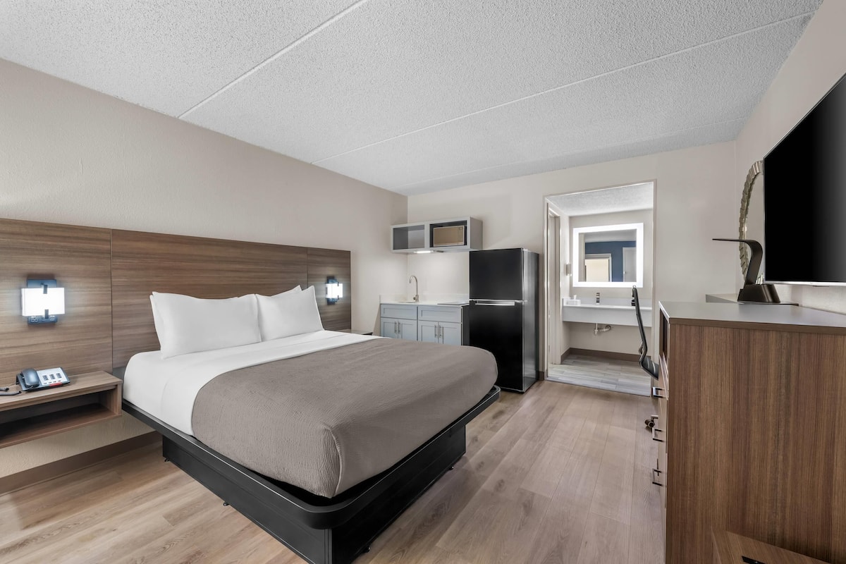 A hotel room with a bed, bedside table, nightstand, desk, chair, and a TV.