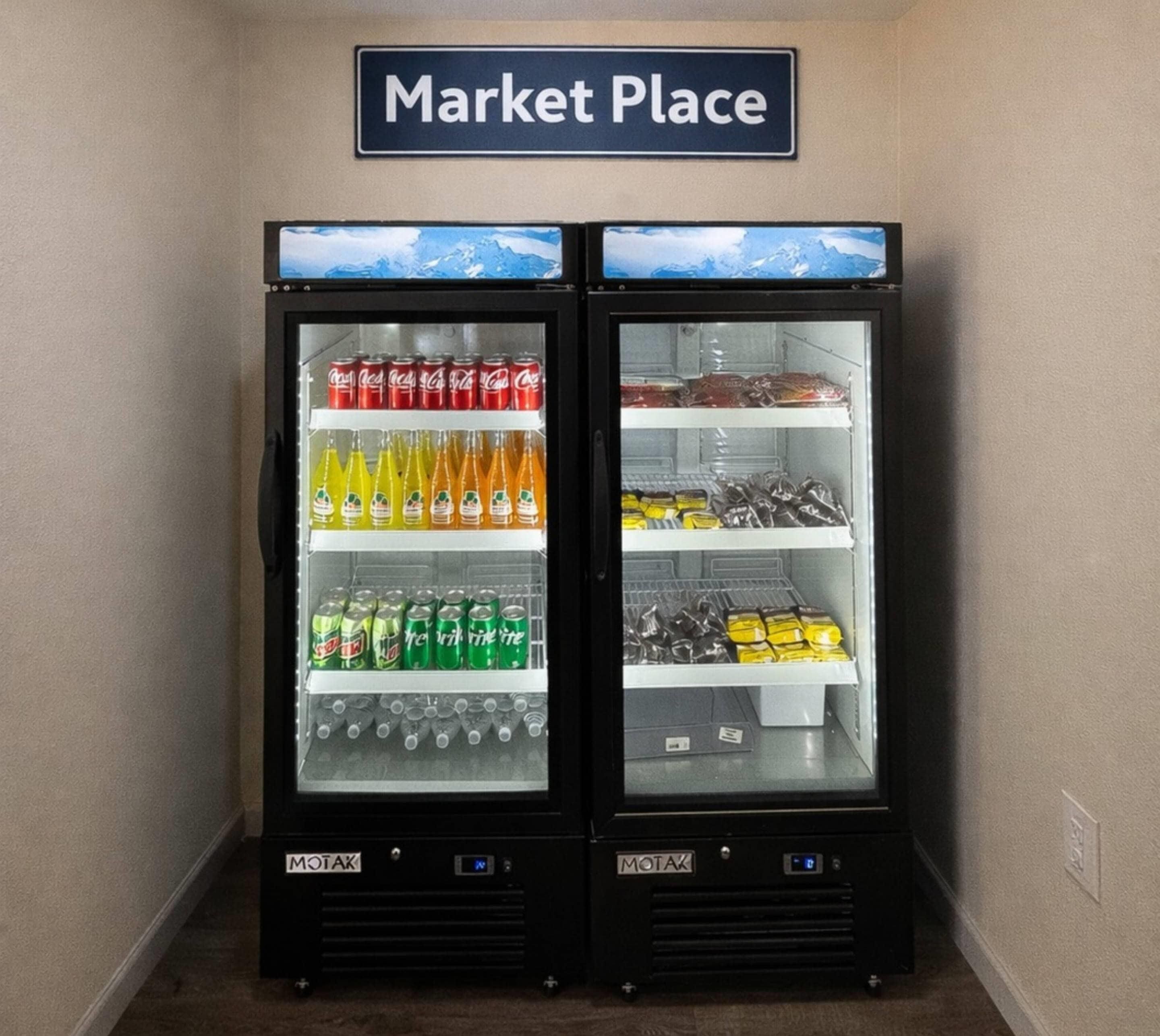 Two vending machines with a 'Market Place' sign above them, stocked with beverages and snacks.