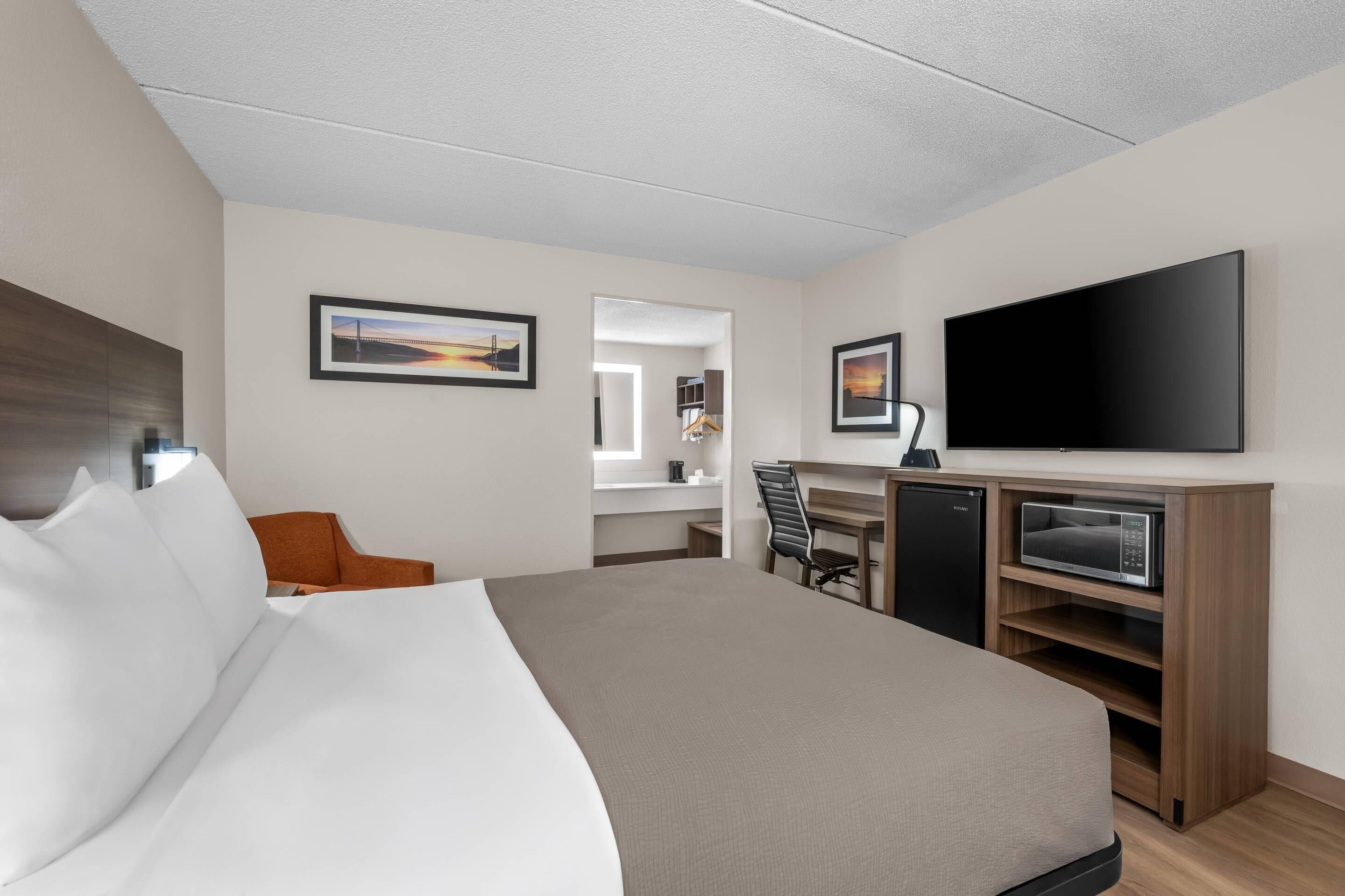 A hotel room with a bed, a desk with a computer, a TV, and a microwave.