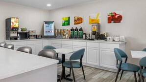 A modern kitchen with a coffee machine, microwave, and various appliances. There are chairs and a table in the dining area.