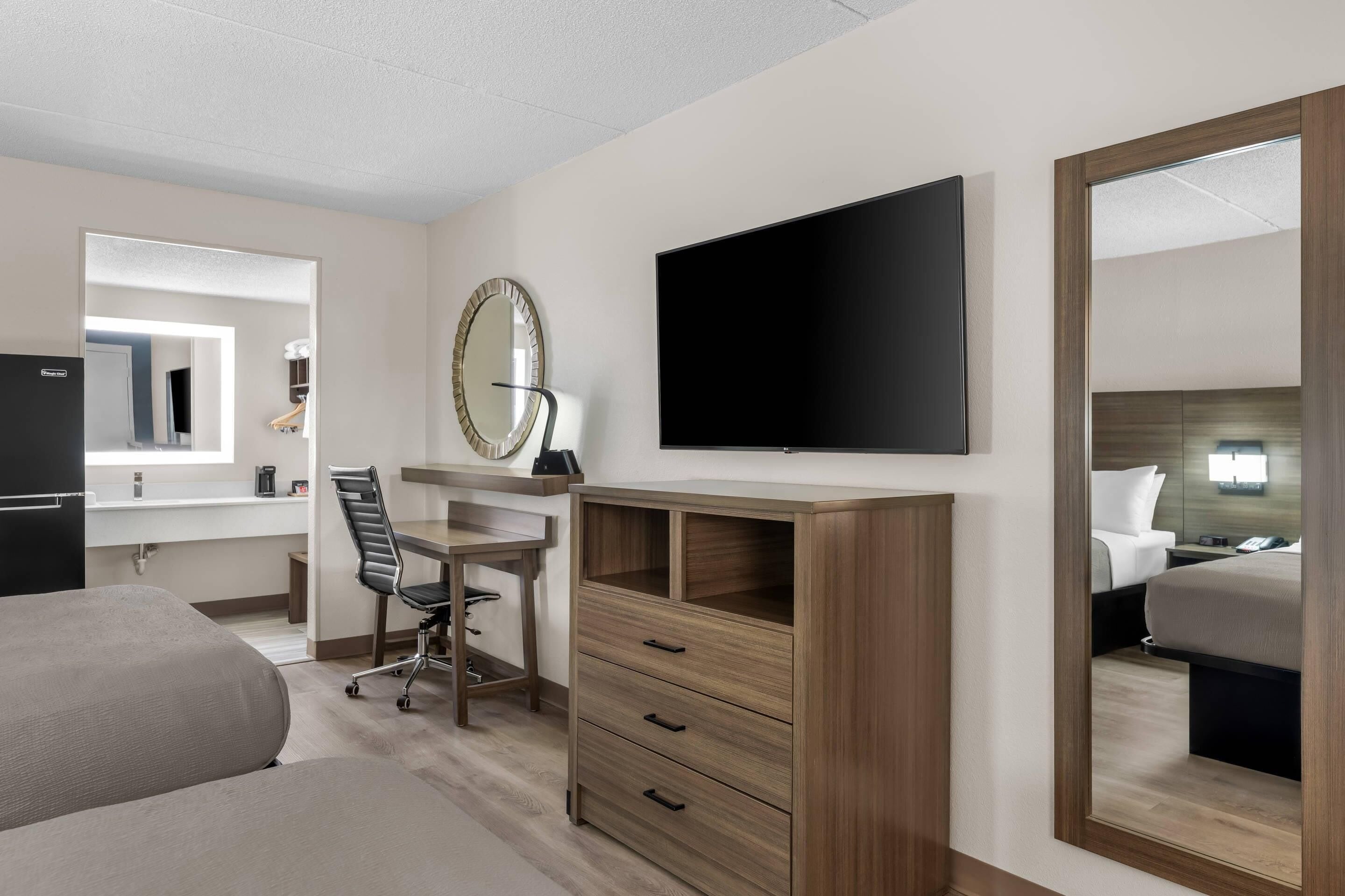 Een hotelkamer met een bed, een bureau met stoel, een televisie, een spiegel en een dressoir.