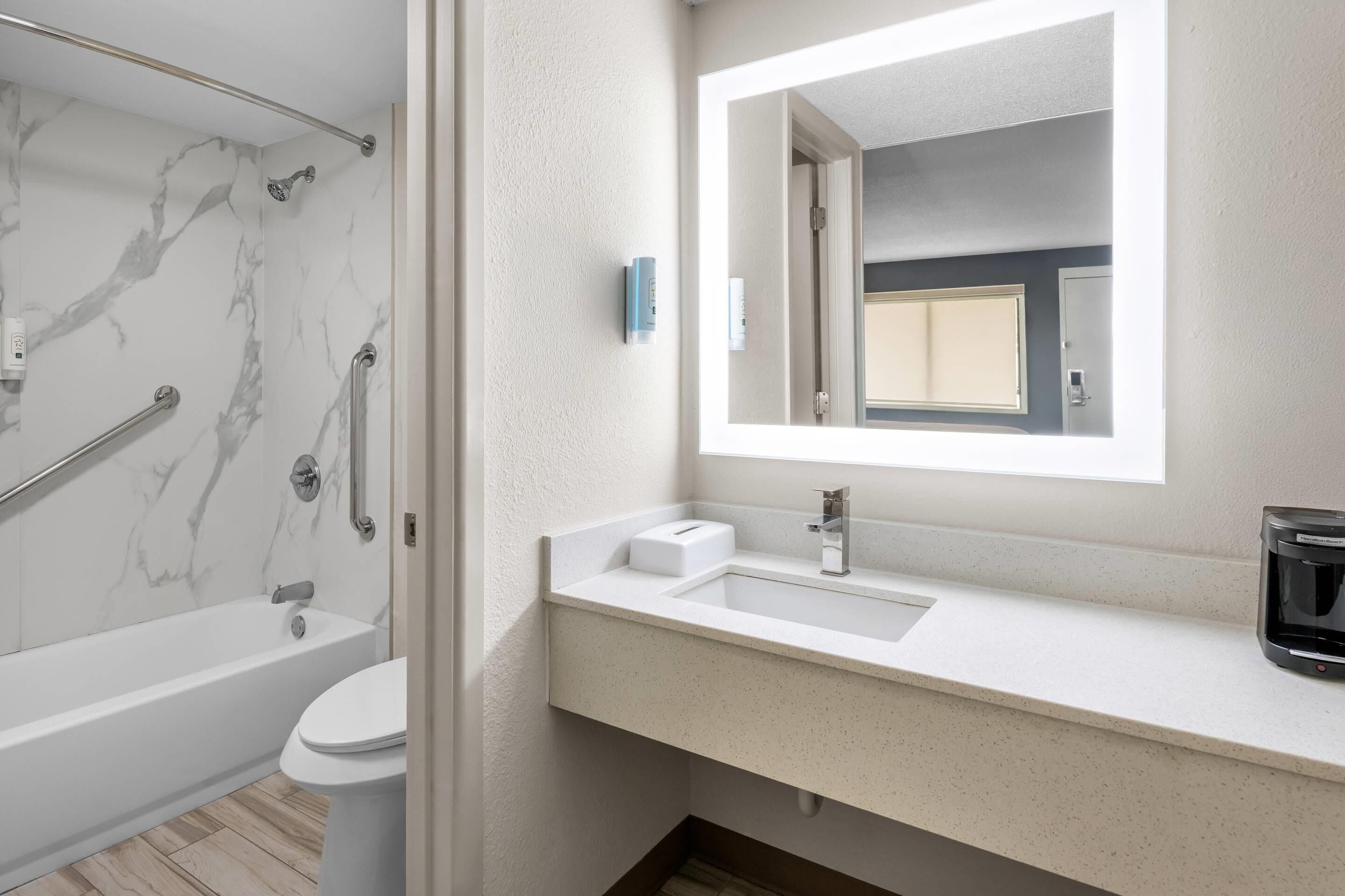 Un baño moderno con ducha de mármol, inodoro blanco, lavamanos con espejo y cafetera.