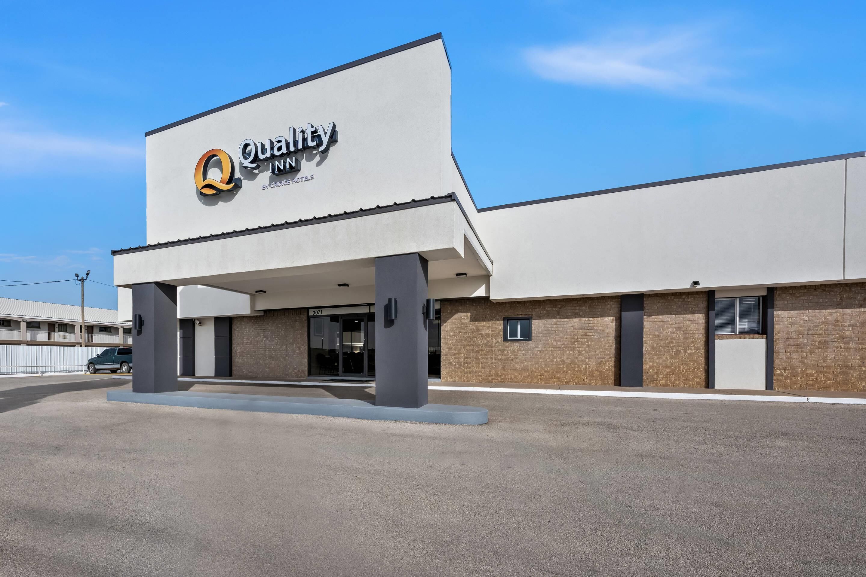 A modern building with a 'Quality Inn' sign, a covered entrance, and a clear sky.
