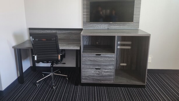 A modern office desk with a built-in monitor, a black office chair, and a storage cabinet. - Scottish Delight Motel (Midland)