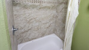 A bathroom with a bathtub, a shower curtain, and a tiled wall. - Scottish Delight Motel (Midland)