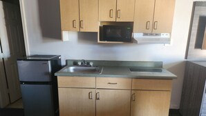 A compact kitchen with wooden cabinets, a stainless steel refrigerator, a microwave, and a sink. - Scottish Delight Motel (Midland)