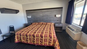 A hotel room with a large bed, a desk, a chair, a window with curtains, and a wall-mounted air conditioner. - Scottish Delight Motel (Midland)