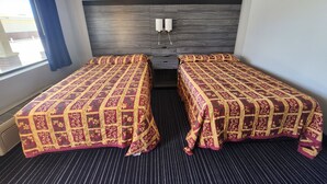 A hotel room with two single beds, a dark wood headboard, a window with blue curtains, and a striped carpet. - Scottish Delight Motel (Midland)