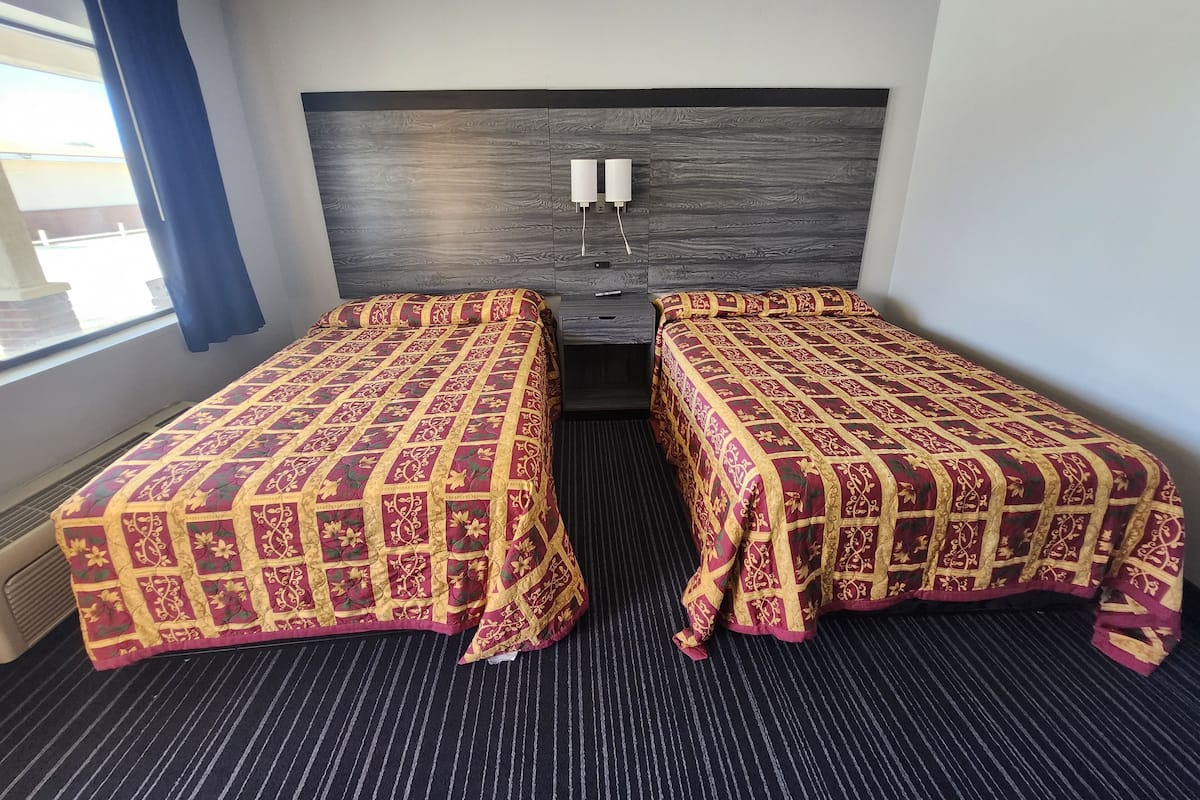Ein Hotelzimmer mit zwei Einzelbetten, einem dunklen Holz-Kopfteil, einem Fenster mit blauen Vorhängen und einem Streifen-Teppich.