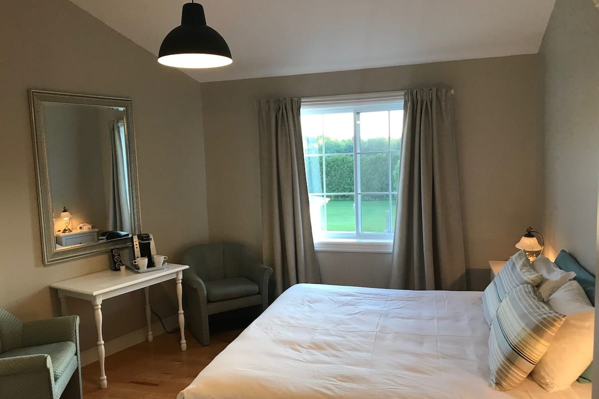 A bedroom with a large bed, a desk, a chair, a mirror, and a window with curtains.