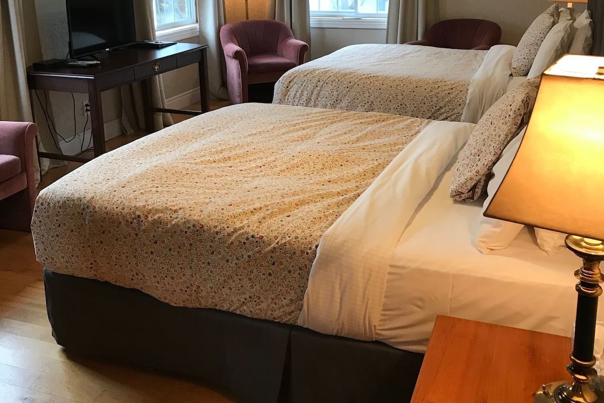 A hotel room with two beds, a desk with a television, a chair, and a lamp.