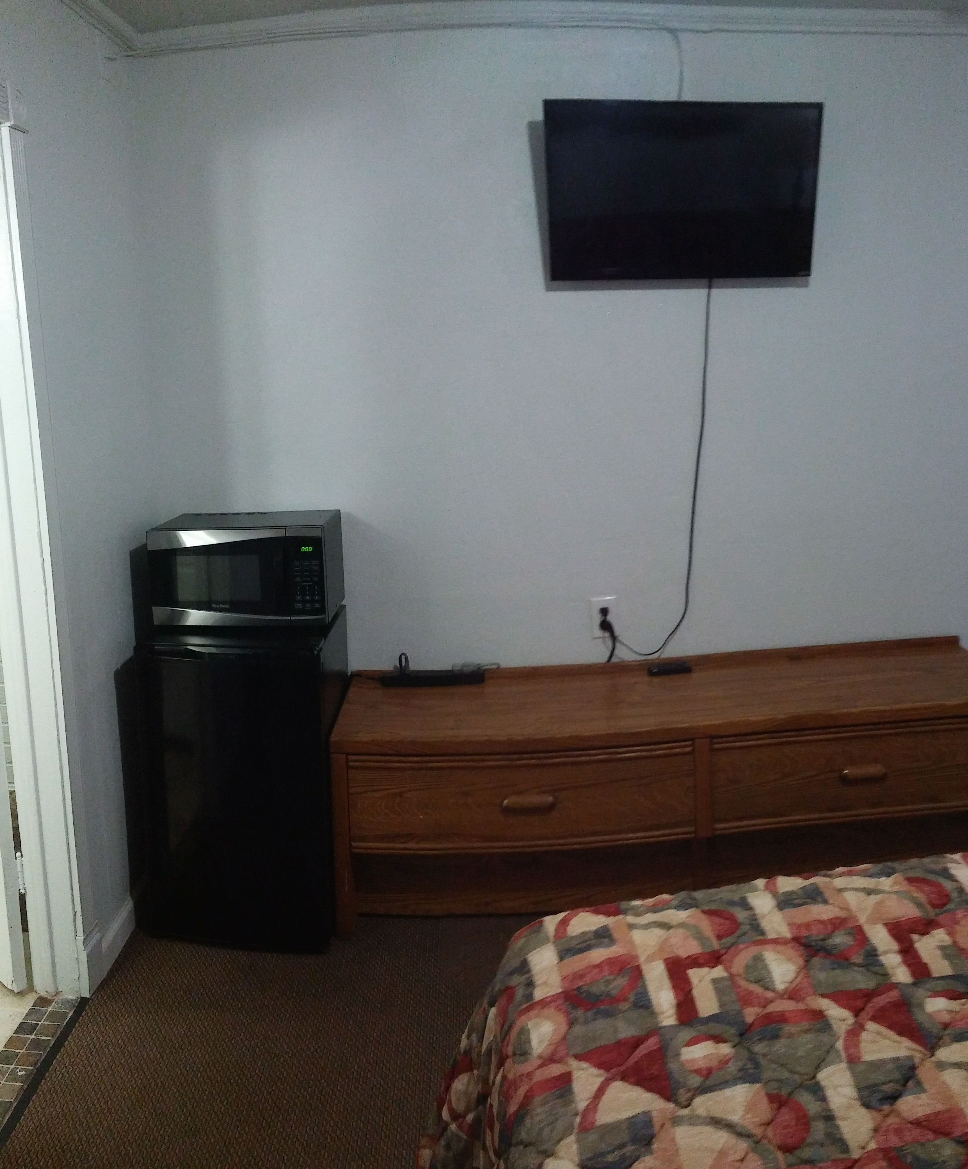 Ein kleines Zimmer mit einer Mikrowelle, einem Holzschrank und einem an der Wand befestigten Fernseher.